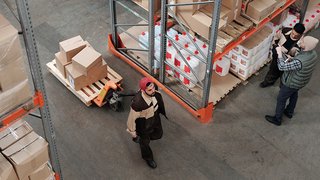 News Lagerarbeiter transportiert Kartons, zwei Kollegen prüfen Liste in Lagerhalle