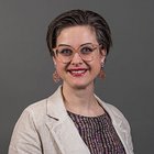 Estetisti Ritratto di donna sorridente con occhiali e giacca beige su sfondo grigio