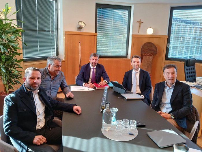 Olympia 2026: Mobilität als gemeinsame Herausforderung Fünf Männer in Anzügen sitzen an einem Konferenztisch in einem Büro