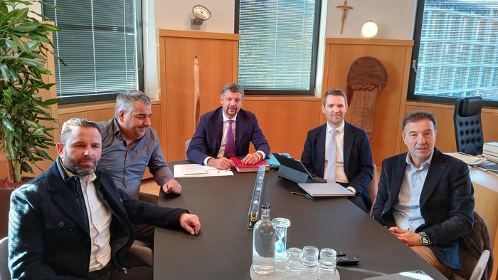 Olimpiadi 2026: la mobilità come sfida comune Cinque uomini in giacca seduti a un tavolo da conferenza in ufficio