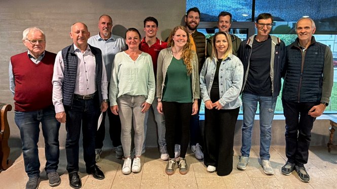 Foto di gruppo di undici persone davanti a una parete grigia all'interno