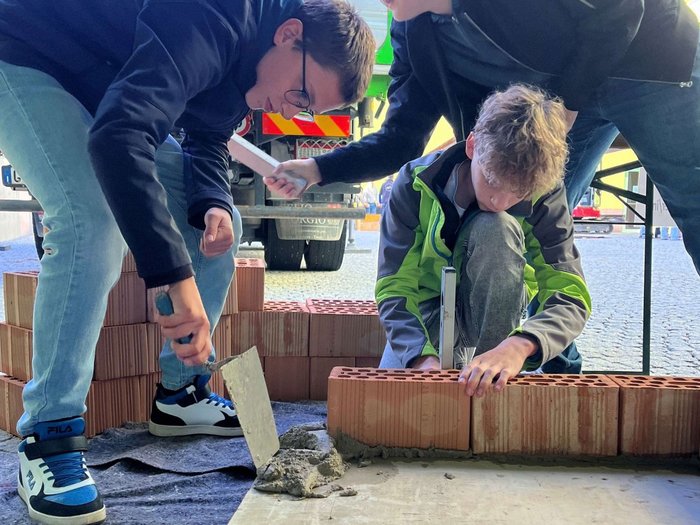 SkillsDay a Vipiteno: Mettersi all’opera Più persone posano mattoni nella malta, una è inginocchiata accanto al muretto