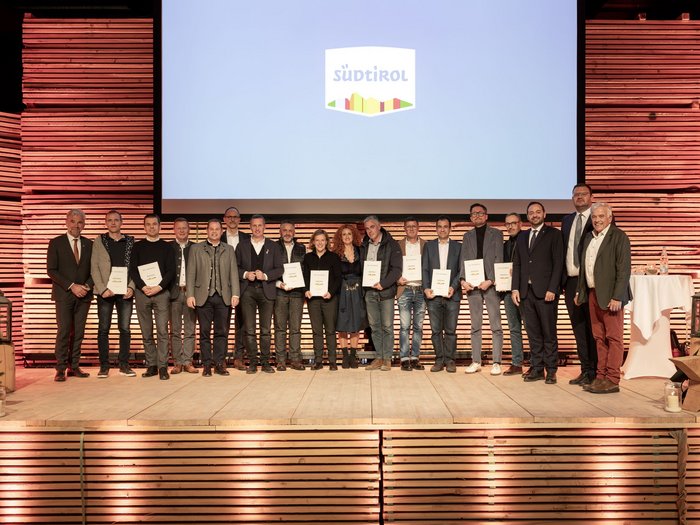 La famiglia del Marchio Alto Adige cresce Foto di gruppo di persone con premi sul palco davanti al logo Sudtirolo