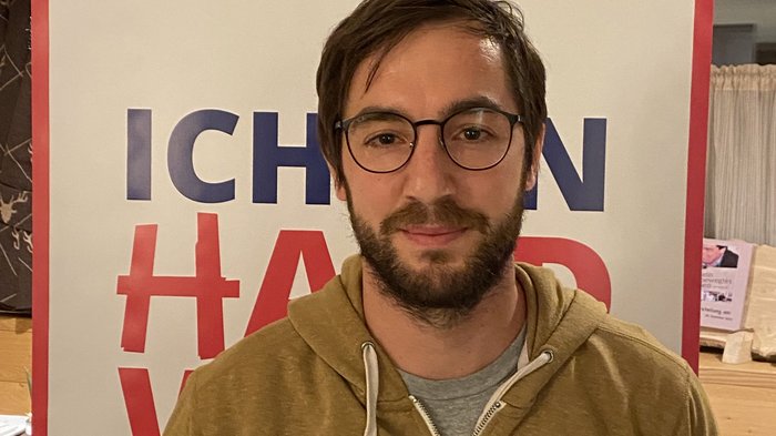 Neuer Handwerkerobmann in Natz-Schabs Mann mit Brille vor Plakat mit Text in Innenraum