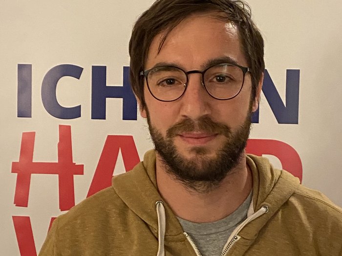 Neuer Handwerkerobmann in Natz-Schabs Mann mit Brille vor Plakat mit Text in Innenraum