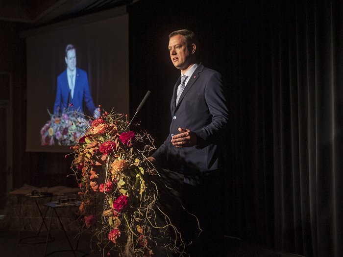 Giornata dell’Artigianato – I giovani come chiave di volta per il nostro futuro Uomo che parla a un leggio decorato con fiori durante un discorso