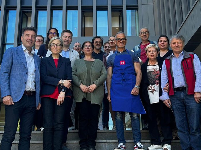 Nuovi spazi, obiettivi comuni: lvh.apa in visita alla Scuola professionale provinciale “Guglielmo Marconi” Foto di gruppo di 16 persone davanti a un edificio moderno