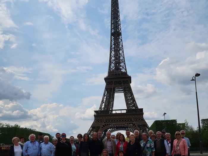 lvh-Seniorinnen und Senioren auf Frühlingsreise: Paris, mon amour! Gruppe von Touristen vor dem Eiffelturm bei bewölktem Himmel