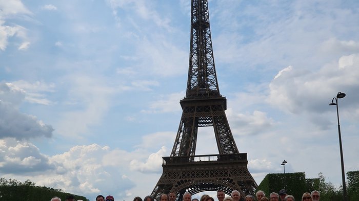 lvh-Seniorinnen und Senioren auf Frühlingsreise: Paris, mon amour! Gruppe von Touristen vor dem Eiffelturm bei bewölktem Himmel