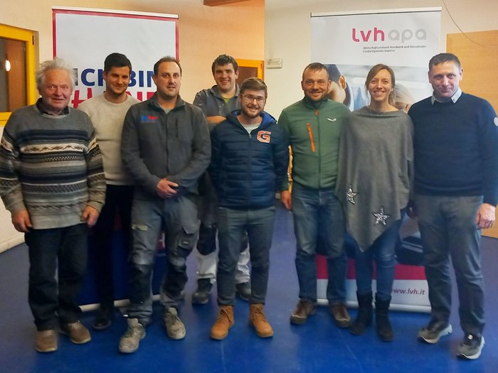 Martin Weiss als Ortsobmann bestätigt Gruppenfoto von acht Personen vor zwei Werbebannern in einem Raum