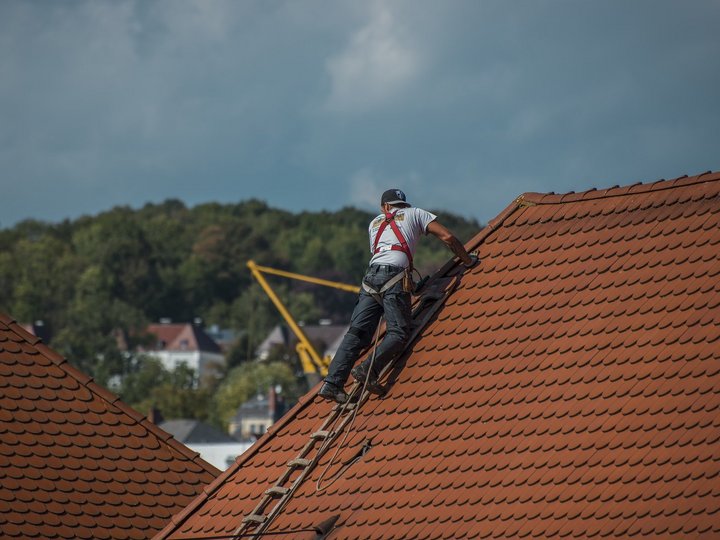 Dachdecker Handwerker repariert Dachziegel auf einem Hausdach an einer Leiter