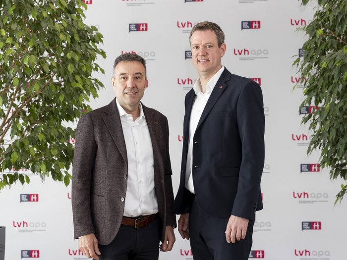 lvh unterzeichnet „Think Small First“-Charta: Starkes Signal für kleine und mittlere Betriebe Zwei Männer im Anzug stehen vor einer lvhapa gesponserten Wand zwischen zwei Pflanzen