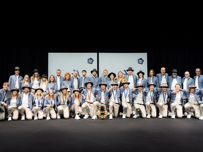 WorldSkills: l’Alto Adige celebra i suoi giovani talenti Gruppo con giacche blu e cappelli sul palco davanti a schermi chiari