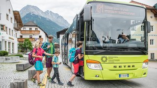 News Familie steigt in grünen Bus in bergiger Stadt mit traditionellen Häusern ein