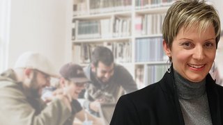 News Frau lächelt vor verschwommenem Hintergrund mit Personen in Bibliothek