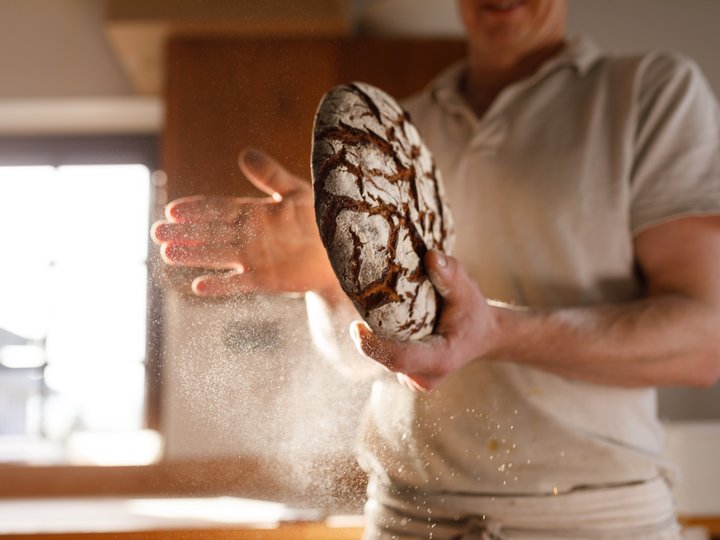 Panettieri Persona tiene pane appena cotto con polvere di farina nell'aria