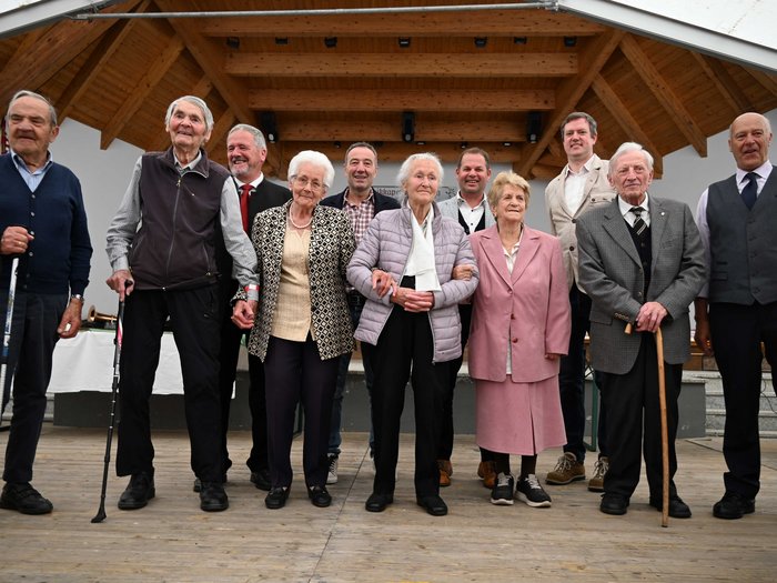61. Althandwerkertreffen in Luttach: ein unvergessliches Erlebnis Gruppe von älteren Menschen und einigen jüngeren Männern auf einer Bühne mit Holzdecke