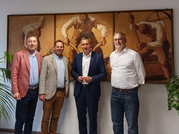 Zukunft des Südtiroler Metzgerhandwerks Vier Männer stehen vor einem dreiteiligen Gemälde mit arbeitenden Figuren