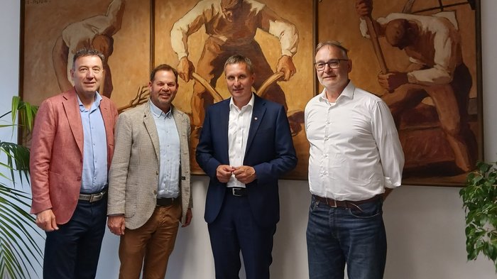 Il futuro della macelleria artigianale in Alto Adige Quattro uomini in piedi davanti a un dipinto tripartito con figure al lavoro