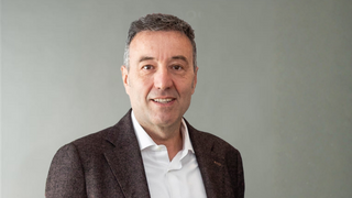 News Ritratto di un uomo sorridente con camicia bianca e giacca scura su sfondo grigio