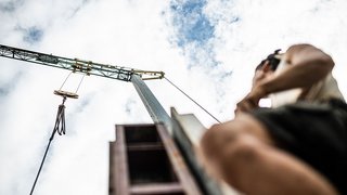 News Blick nach oben auf einen Kran und eine Person vor bewölktem Himmel