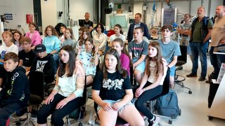 News Schüler und Erwachsene sitzen und stehen in einem modernen Klassenzimmer bei einer Präsentation