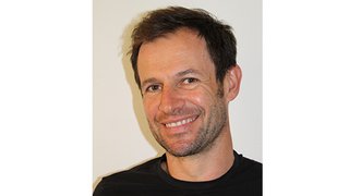 News Porträt eines lächelnden Mannes mit kurzem dunklem Haar vor weißem Hintergrund