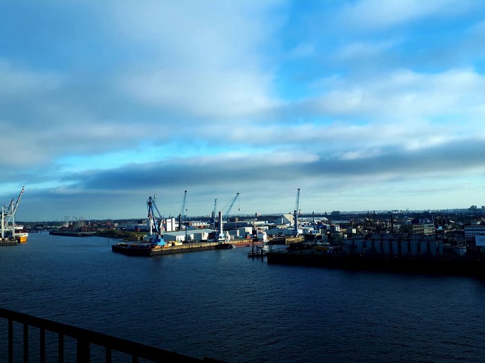 Die Althandwerker besuchen Hamburg Hafen mit Kränen, Lagerhäusern und Schiffen unter bewölktem blauen Himmel