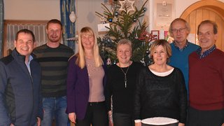 News Gruppe von sieben Personen steht vor einem Weihnachtsbaum in einem Raum