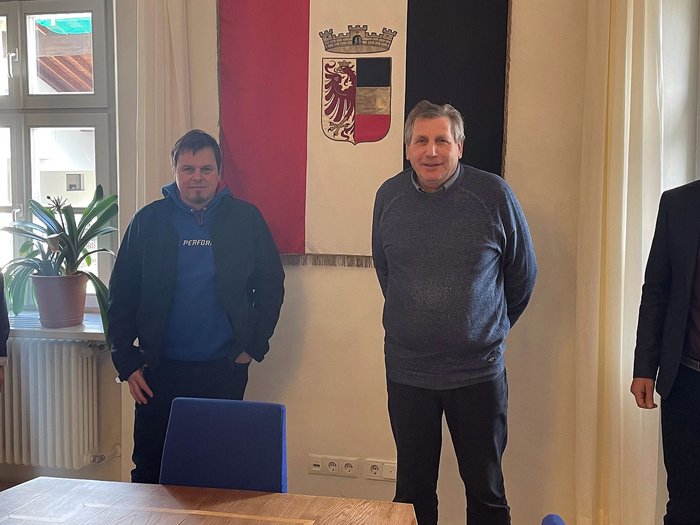 Aufträge für das Handwerk Vier Männer stehen vor einer Wand mit einem Wappen in einem hellen Raum