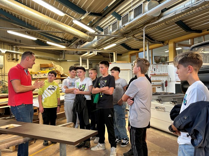 Entdeckungsreise in Berufe des Handwerks und Gastgewerbes an der Mittelschule St. Martin in Passeier Ein Mann erklärt einer Gruppe Jugendlicher in einer Werkstatt etwas