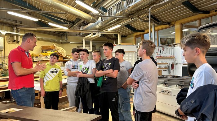 Entdeckungsreise in Berufe des Handwerks und Gastgewerbes an der Mittelschule St. Martin in Passeier Ein Mann erklärt einer Gruppe Jugendlicher in einer Werkstatt etwas