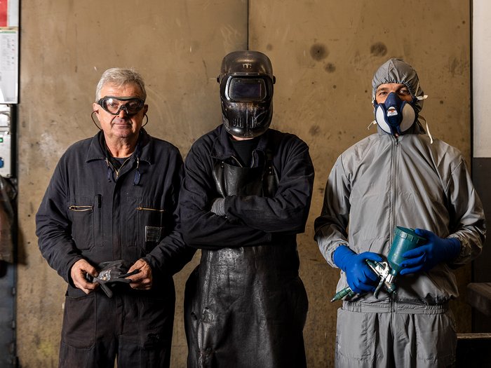 La sicurezza è un lavoro fatto a mano Tre operai con diversi abiti protettivi in un'officina davanti a un muro