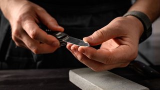 News Uomo affila coltello pieghevole su pietra per affilare