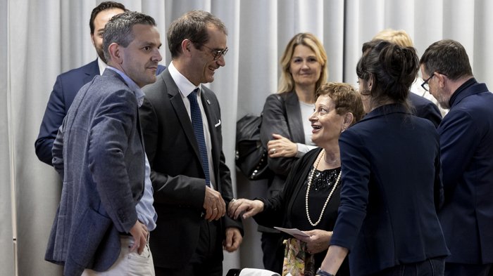 Südtiroler Meisterbund: neuer Rat der Meister gewählt Mehrere Personen im Gespräch bei einer formellen Veranstaltung vor grauem Vorhang