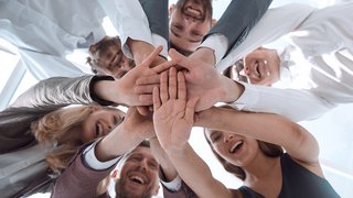 News Fröhliches Team steht im Kreis und legt Hände zusammen