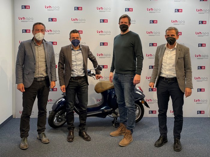 Prosegue la cooperazione tra STA ed lvh.apa Quattro uomini con mascherine davanti a sfondo lvh apa con scooter