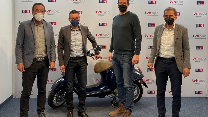 STA und lvh weiterhin auf Kooperationskurs Vier Männer mit Masken posieren vor lvh apa Hintergrund mit Roller