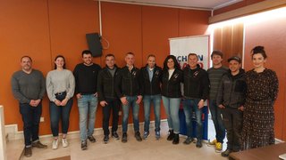 News Gruppe von elf Personen posiert vor oranger Wand in Innenraum