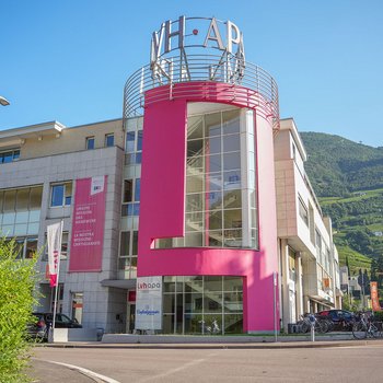 Der lvh im Überblick Gebäude mit rotem Turm und Schriftzug bei klarem Himmel und Bergen im Hintergrund