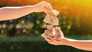 © Shutterstock Hände mit kleinen Geldsäcken bei Sonnenuntergang im Freien