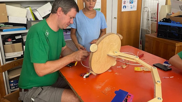 Kids Academy 2024: è la volta di Merano! Uomo e ragazzo lavorano a progetto meccanico in legno su tavolo in officina