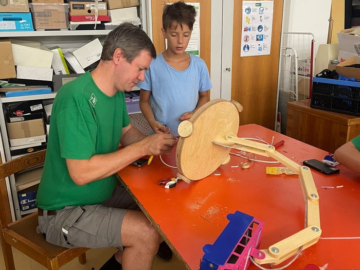 Kids-Academy 2024: lichtes Treiben in Meran Mann und Junge arbeiten an Holz-Mechanikprojekt am Tisch in Werkstatt