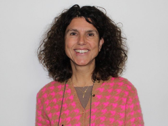 Umbruch bei den Berufsgemeinschaften der Karosserietechniker/innen und KFZ-Mechatroniker/innen Lächelnde Frau mit lockigem Haar und rosa kariertem Pullover vor weißem Hintergrund