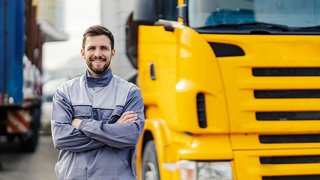 News Lächelnder Lkw-Fahrer in Arbeitskleidung vor gelbem Lastwagen