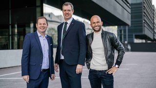 News Drei Männer, zwei in Anzügen und einer in Lederjacke, vor modernem Gebäude