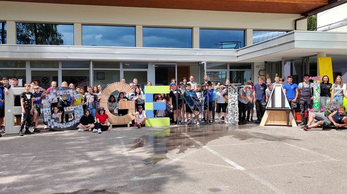 Handwerk und Tourismus: erfolgreiches Schuljahr abgeschlossen Große Gruppe von Menschen steht hinter großen Buchstaben in einem Hof