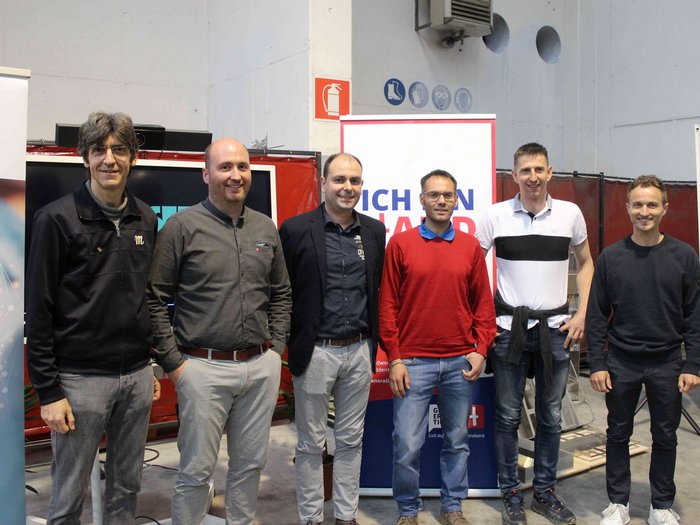 Jahresversammlung bringt viel Neues Sechs Männer stehen nebeneinander in einer Halle vor Werbebannern