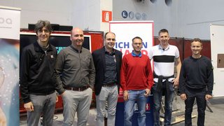 News Sechs Männer stehen nebeneinander in einer Halle vor Werbebannern