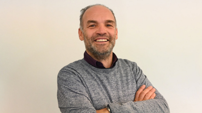Home Uomo sorridente con le braccia incrociate e un maglione grigio su sfondo chiaro